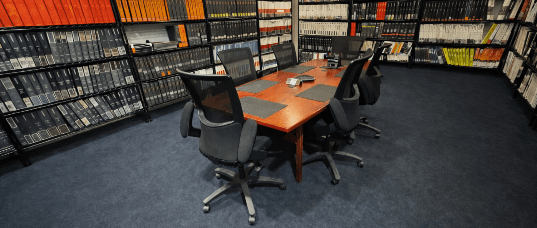 Conference room with black swivel chairs and a wooden table surrounded by bookshelves.